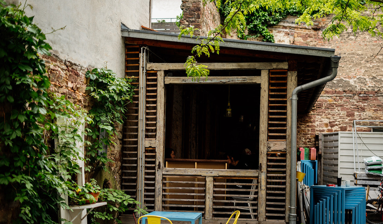 Innenhof der Kulturküche mit hölzerner Veranda. An der Mauer sind grüne Kletterpflanzen.