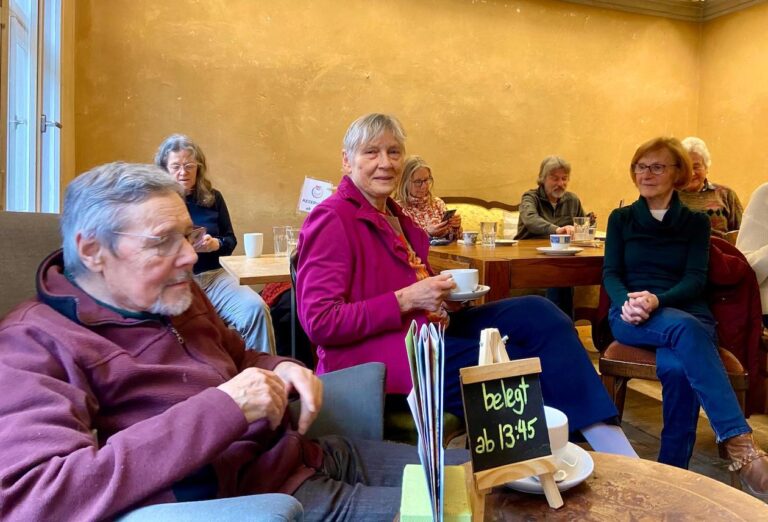 Menschen sitzen in einem Raum der Kulturküche und unterhalten sich. Außerdem trinken sie Kaffee.
