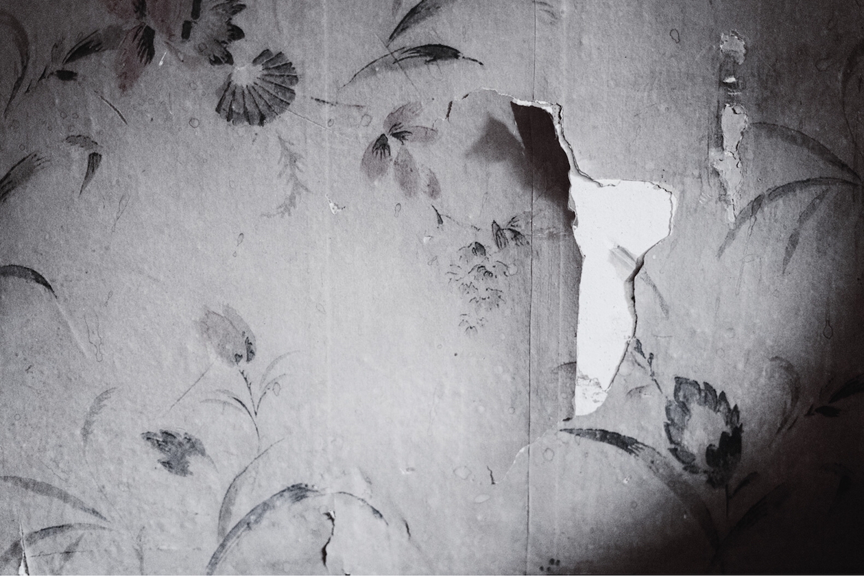 Tapete mit Blumenmuster, ein Teil der Tapete löst sich.
